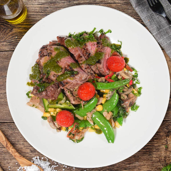 Signature meal of grass-fed ribeye steak with chimichurri and seasonal greens on a plate, served with starch and vegetables.